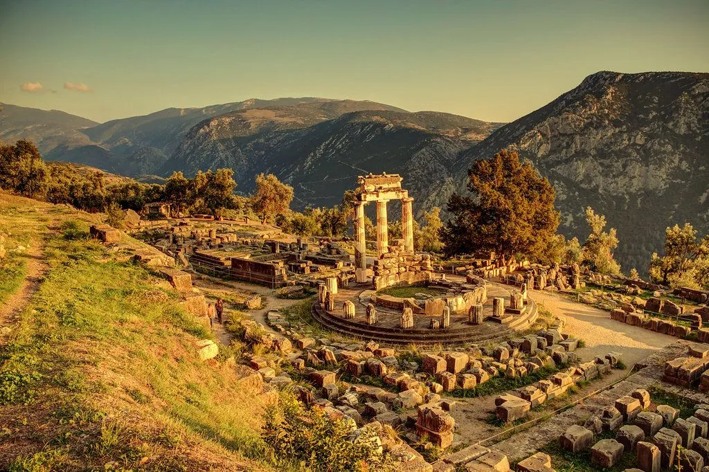 Sunlit ancient ruins of Delphi with stone columns and mountainous backdrop under clear sky.