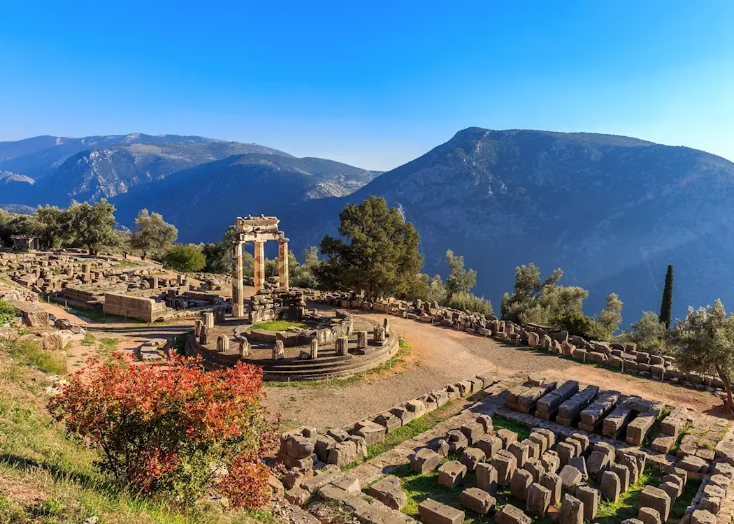 Ancient ruins of a circular temple with mountains and blue sky in the background.