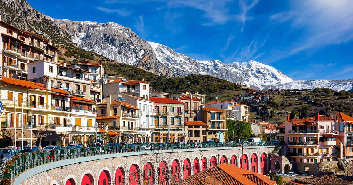 Mountain town with snow-capped peaks in the background and colorful buildings along a curved stone wall.
