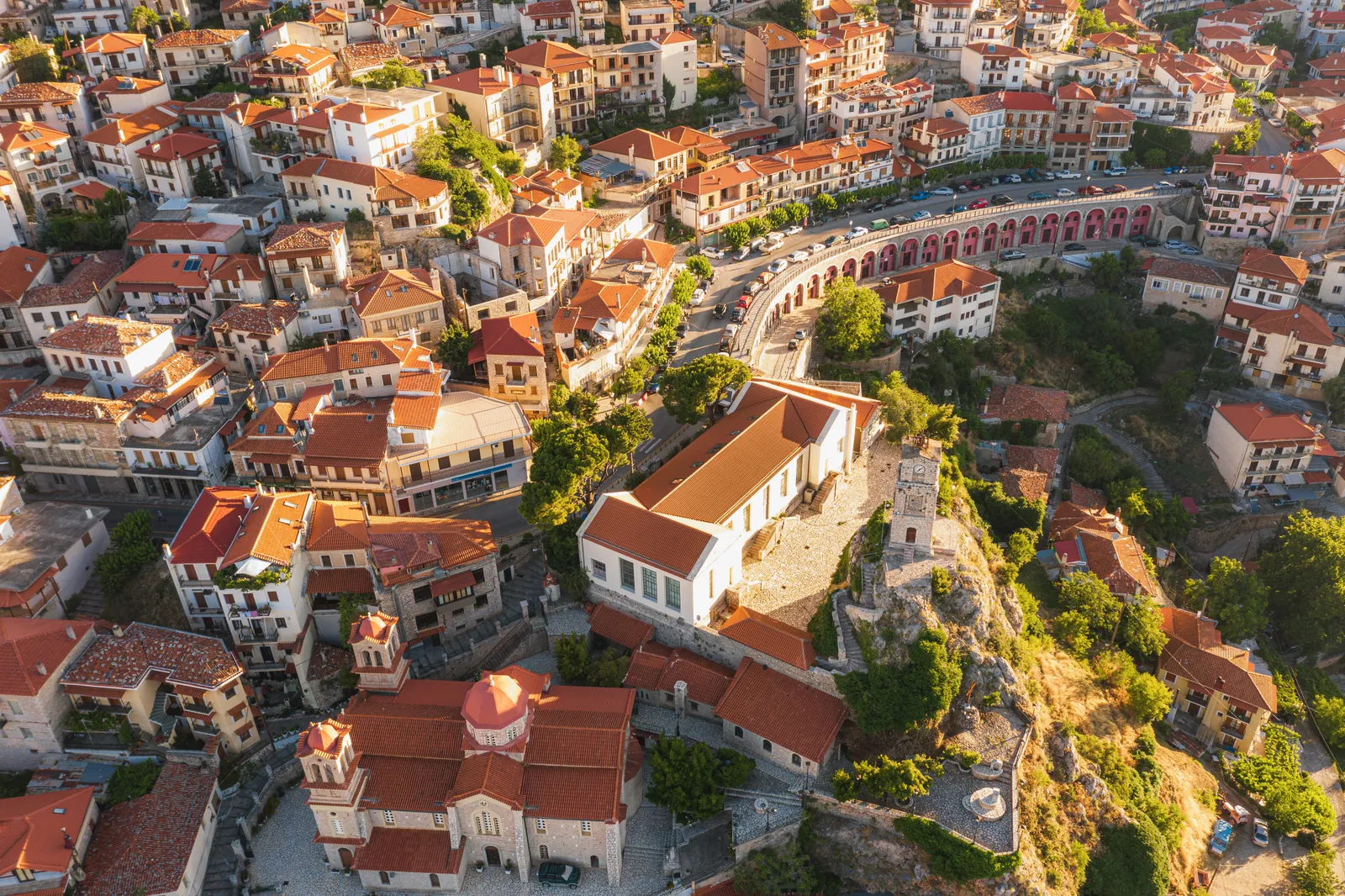 Aerial view of a Mediterranean town with terracotta-roofed buildings, a church, and a stone clock tower on a hill.