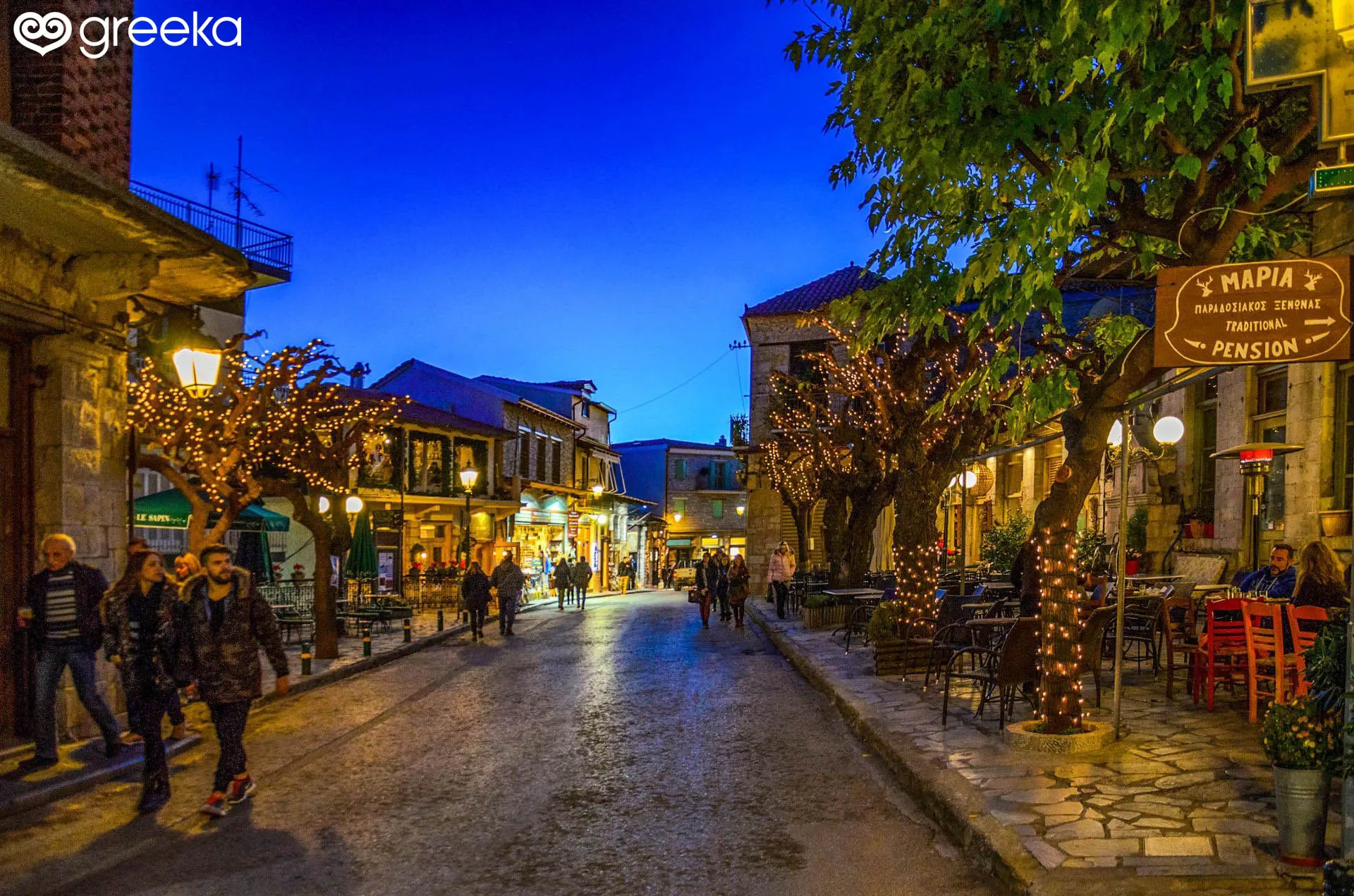 Evening street scene in Arachova with lit trees, people walking, and outdoor seating at cafes.