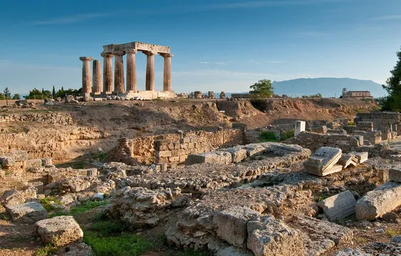 Ancient Greek ruins with standing columns and scattered stone blocks under a blue sky.