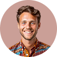 Smiling young man with short brown hair wearing a colorful patterned shirt against a muted pink background.