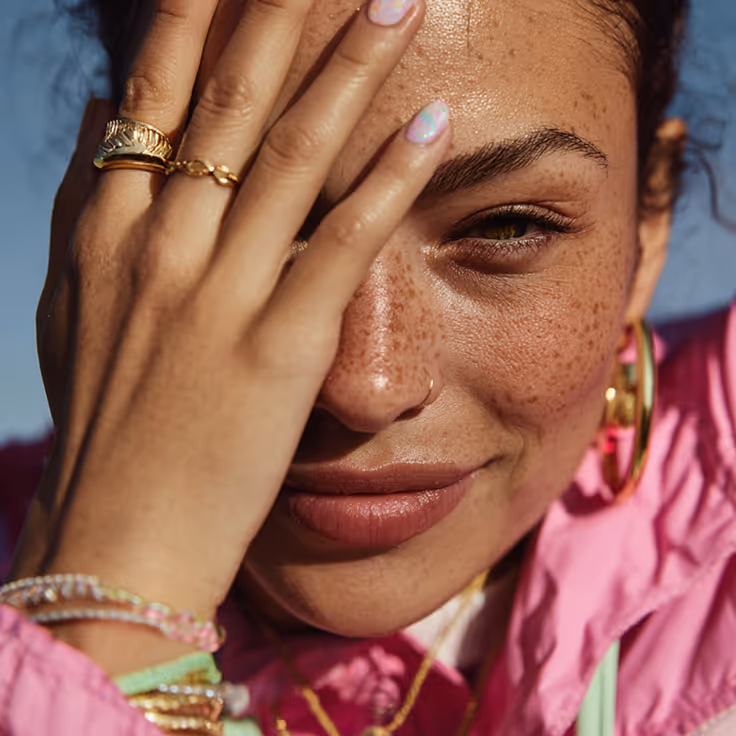 A lady wearing a pink jacket covering one eye with full glam makeup