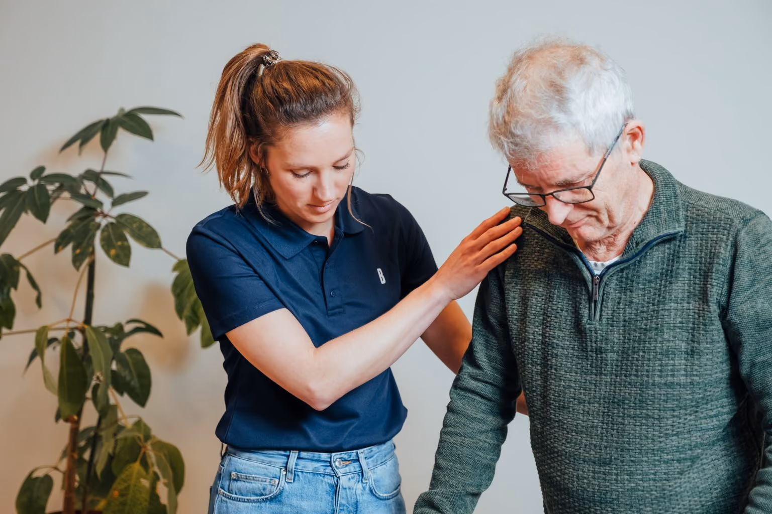 Jonge vrouw helpt oudere man en legt haar hand op zijn schouder ter ondersteuning.