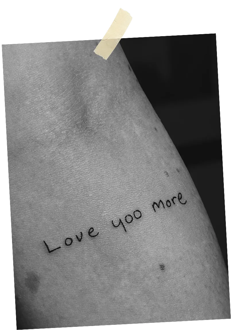 Close-up of a tattoo on skin that reads 'Love yoo more' in simple handwriting.