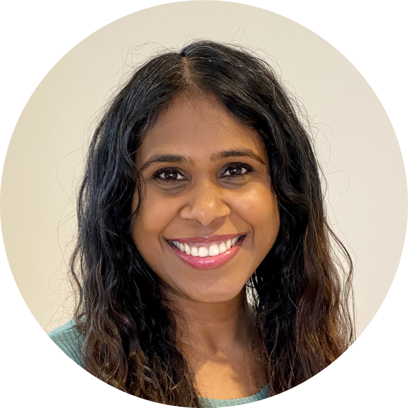 Smiling woman with long curly dark hair wearing a green top, against a plain light background.