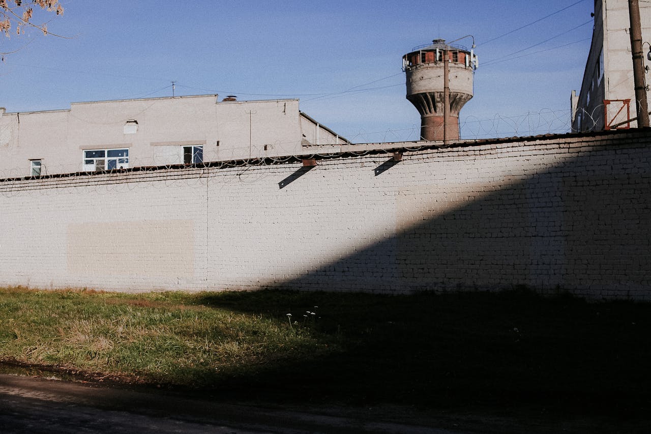 High prison wall topped with barbed wire and a guard tower under a clear sky.
