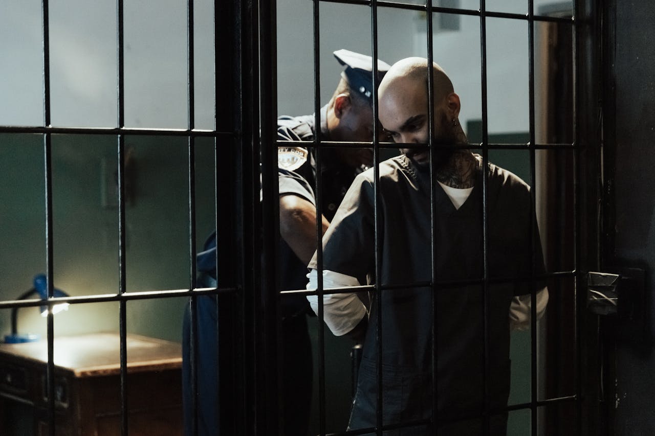 Police officer handcuffing a detainee inside a jail cell behind bars.