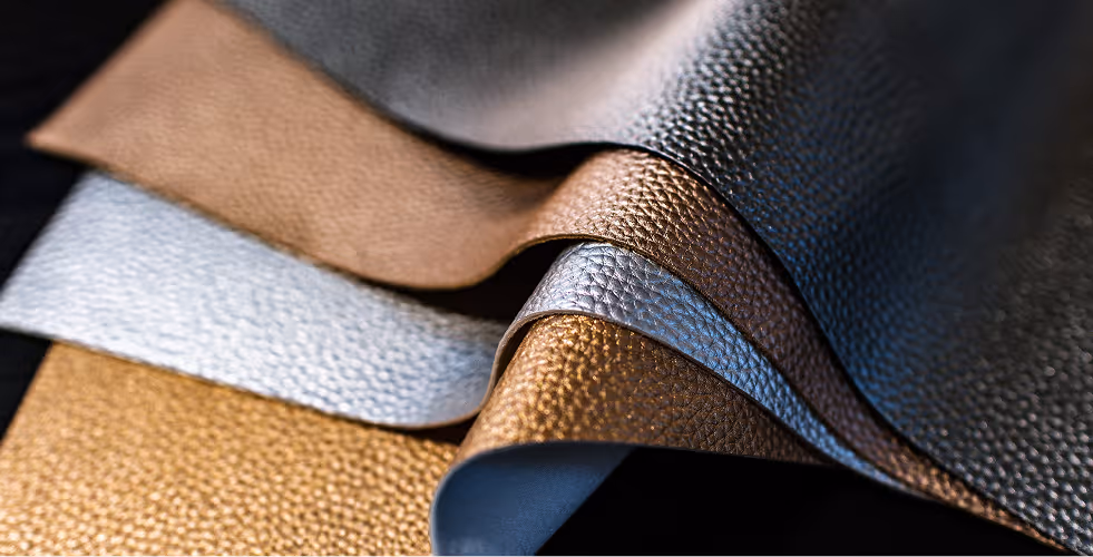 Close-up of layered metallic textured fabric swatches in gold, silver, bronze, and black.
