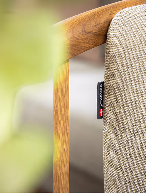 Close-up of a beige textured sofa cushion with a wooden armrest and a fabric label attached.