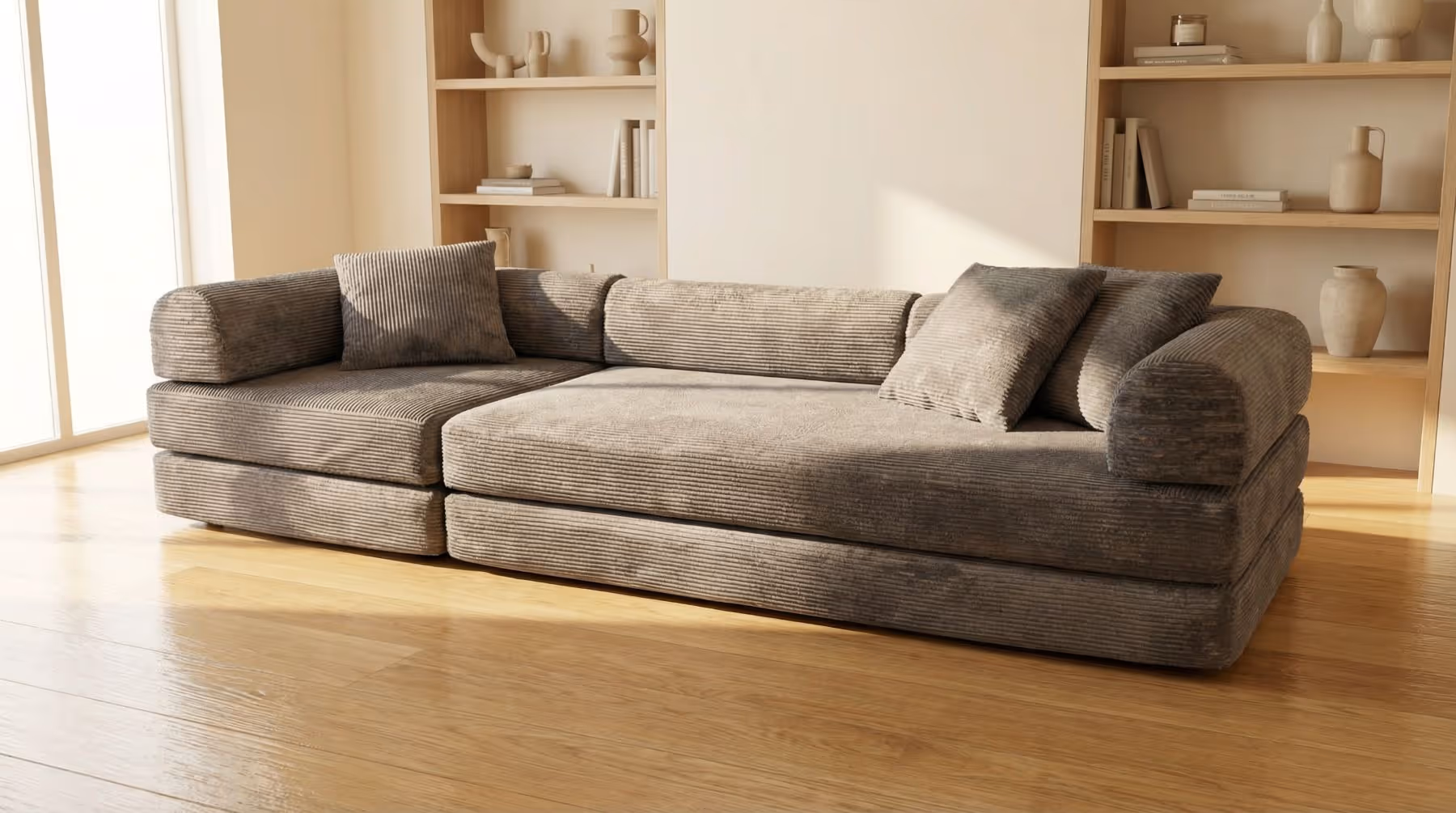 Modern gray corduroy sectional sofa with cushions in a sunlit room with wooden floor and shelves.