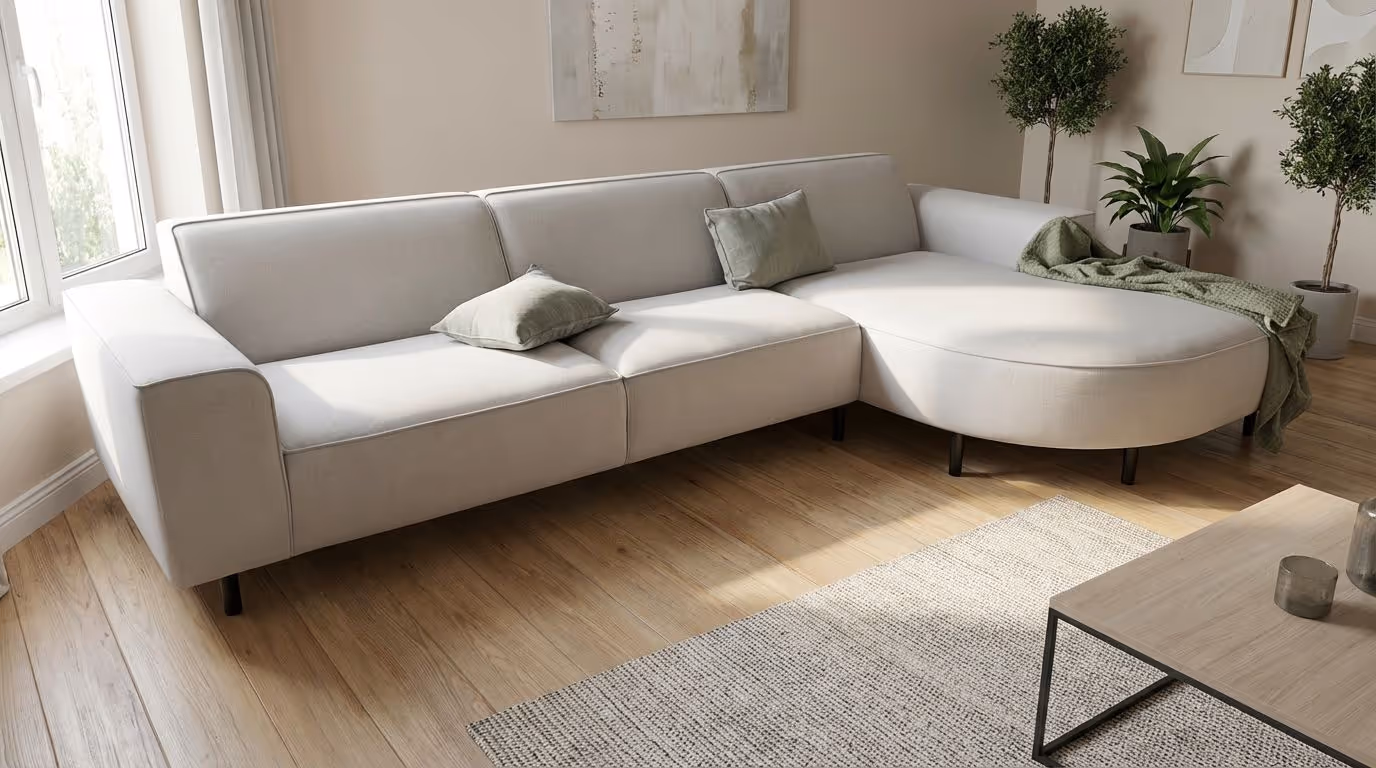 Light gray L-shaped sofa with green pillows and a throw blanket in a sunlit living room with wooden floor, plants, and a coffee table.