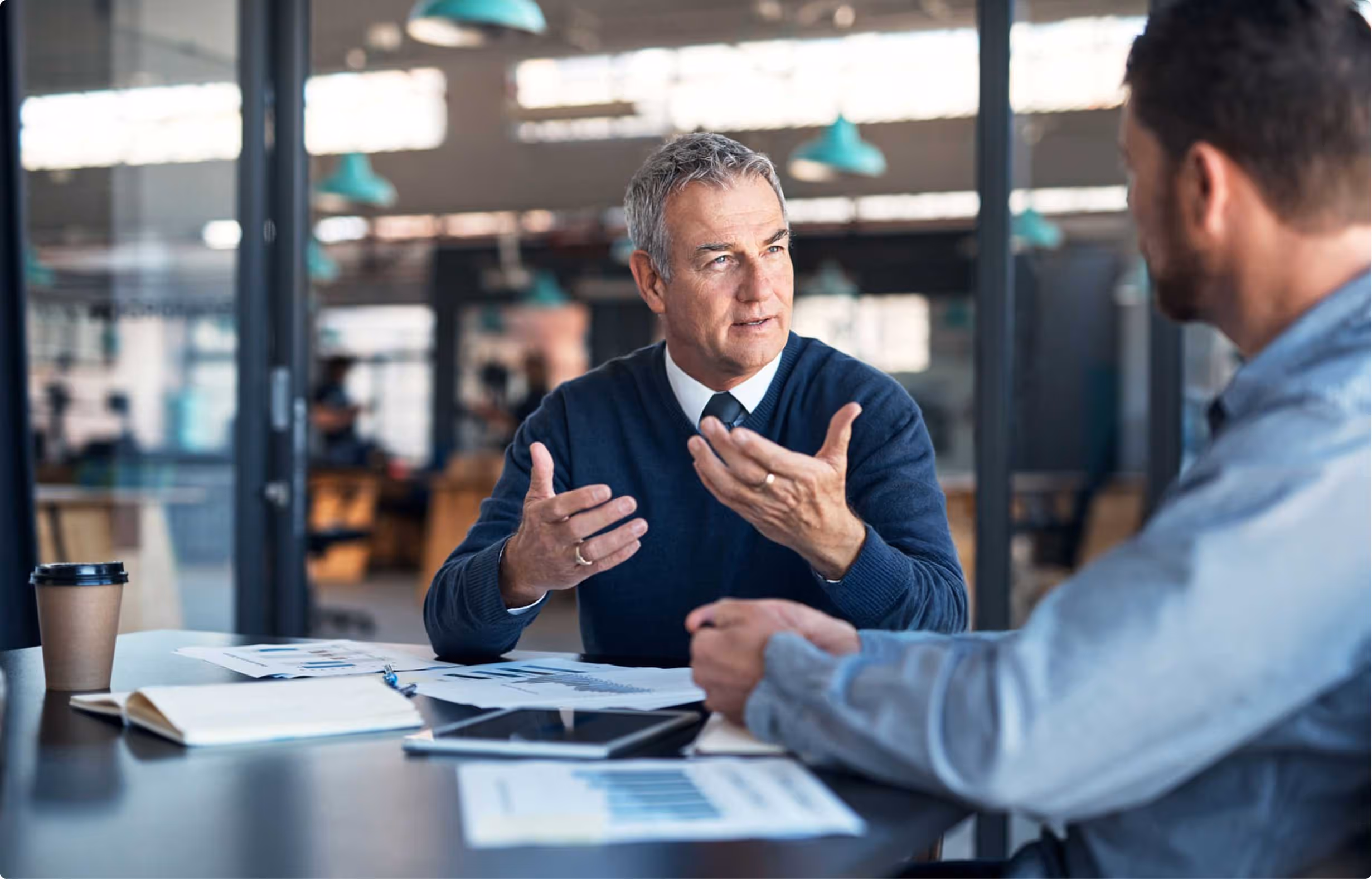 Two men discussing business documents at a table in an office setting.
