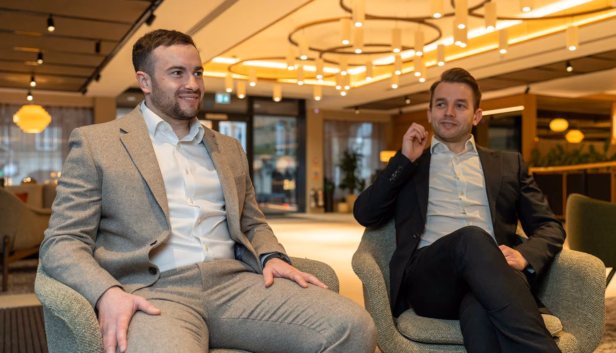 Ben Robinson founder and director and Neil watts director of GRTS in business suits sitting and conversing in a modern, well-lit lounge area.