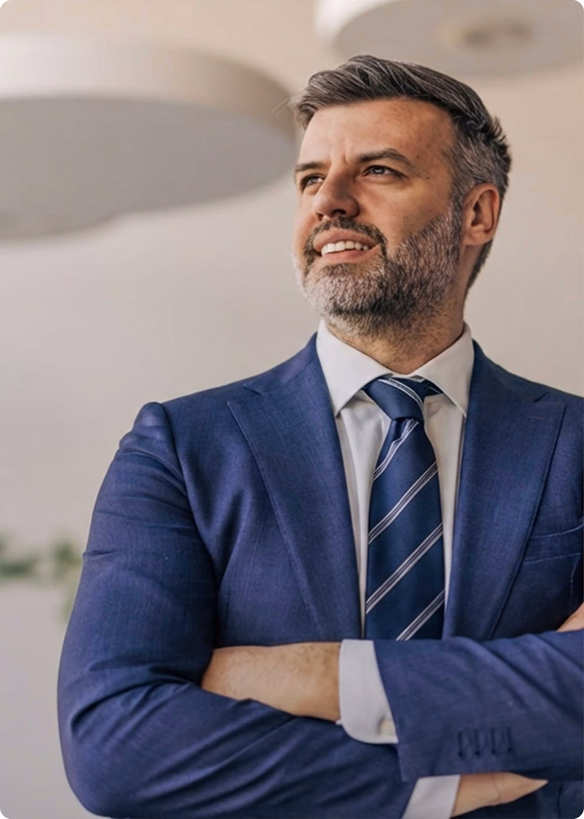 Confident businessman with folded arms wearing a blue suit and striped tie looking to the side.