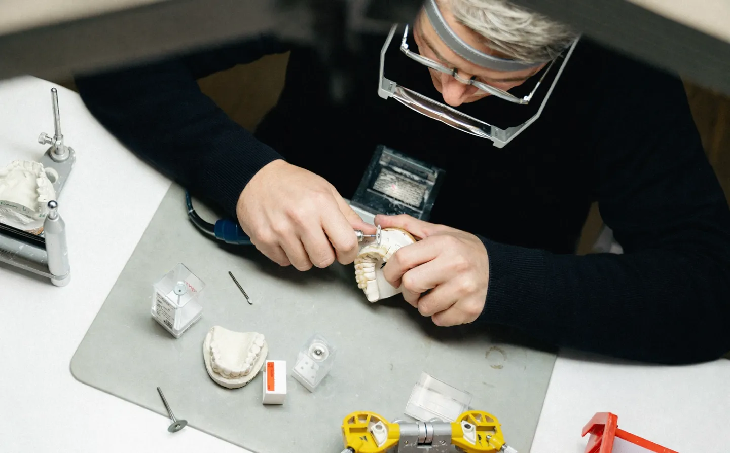 Zahntechniker bearbeitet ein Zahnmodell mit einem Fräser an einem Arbeitsplatz.