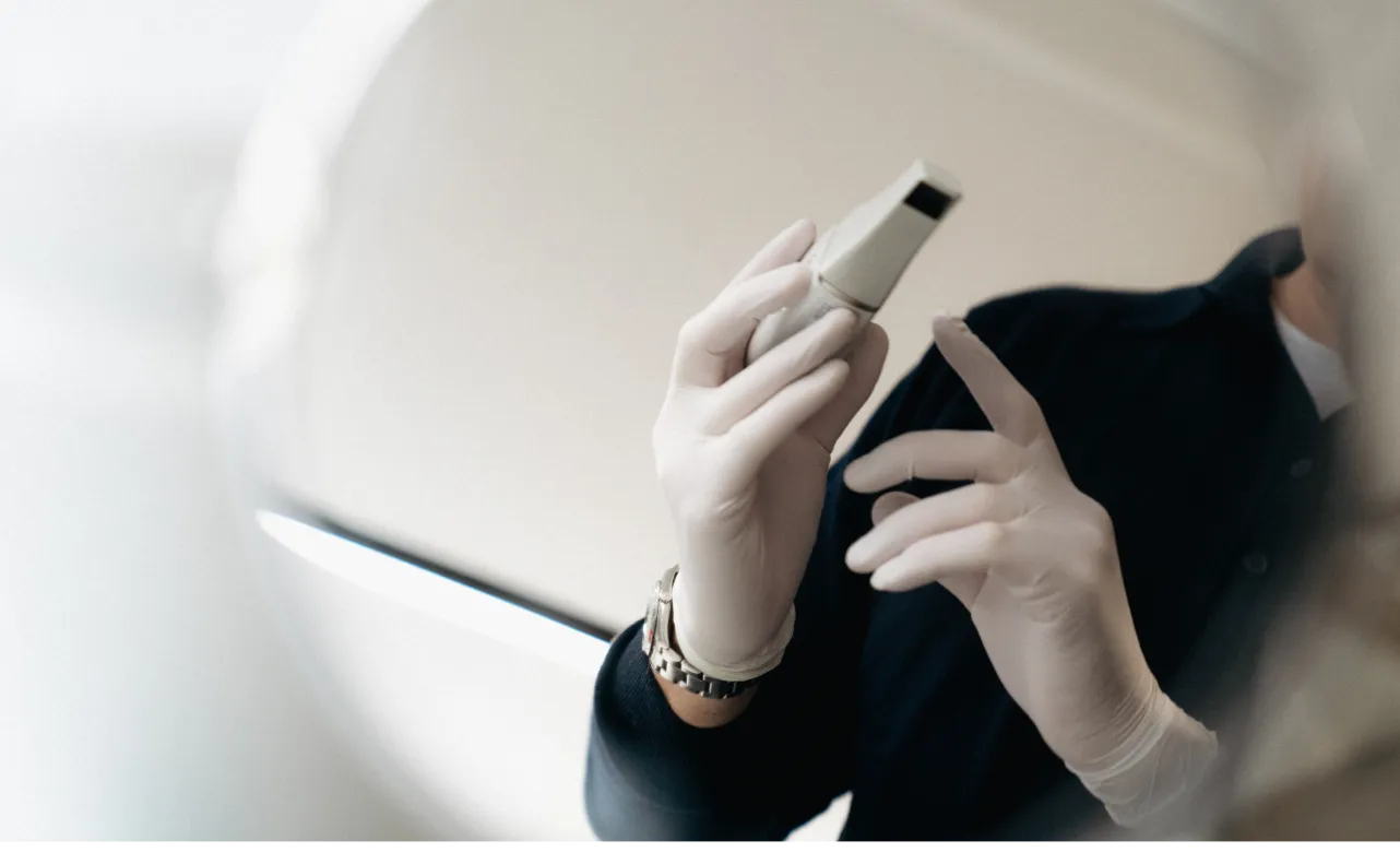 Person trägt weiße Handschuhe und hält ein medizinisches Ultraschallgerät.