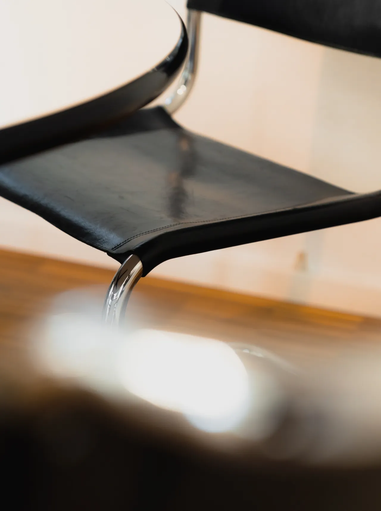 Nahaufnahme eines schwarzen Lederstuhls mit Metallrahmen neben einem runden weißen Tisch.