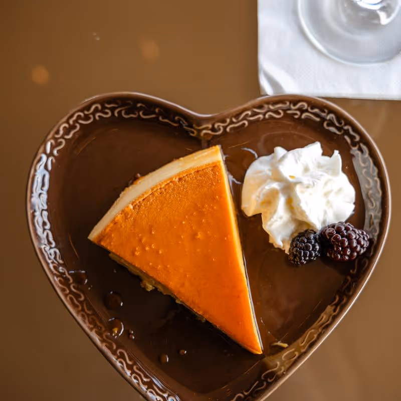 Slice of pumpkin pie with whipped cream and two blackberries on a decorative heart-shaped plate.