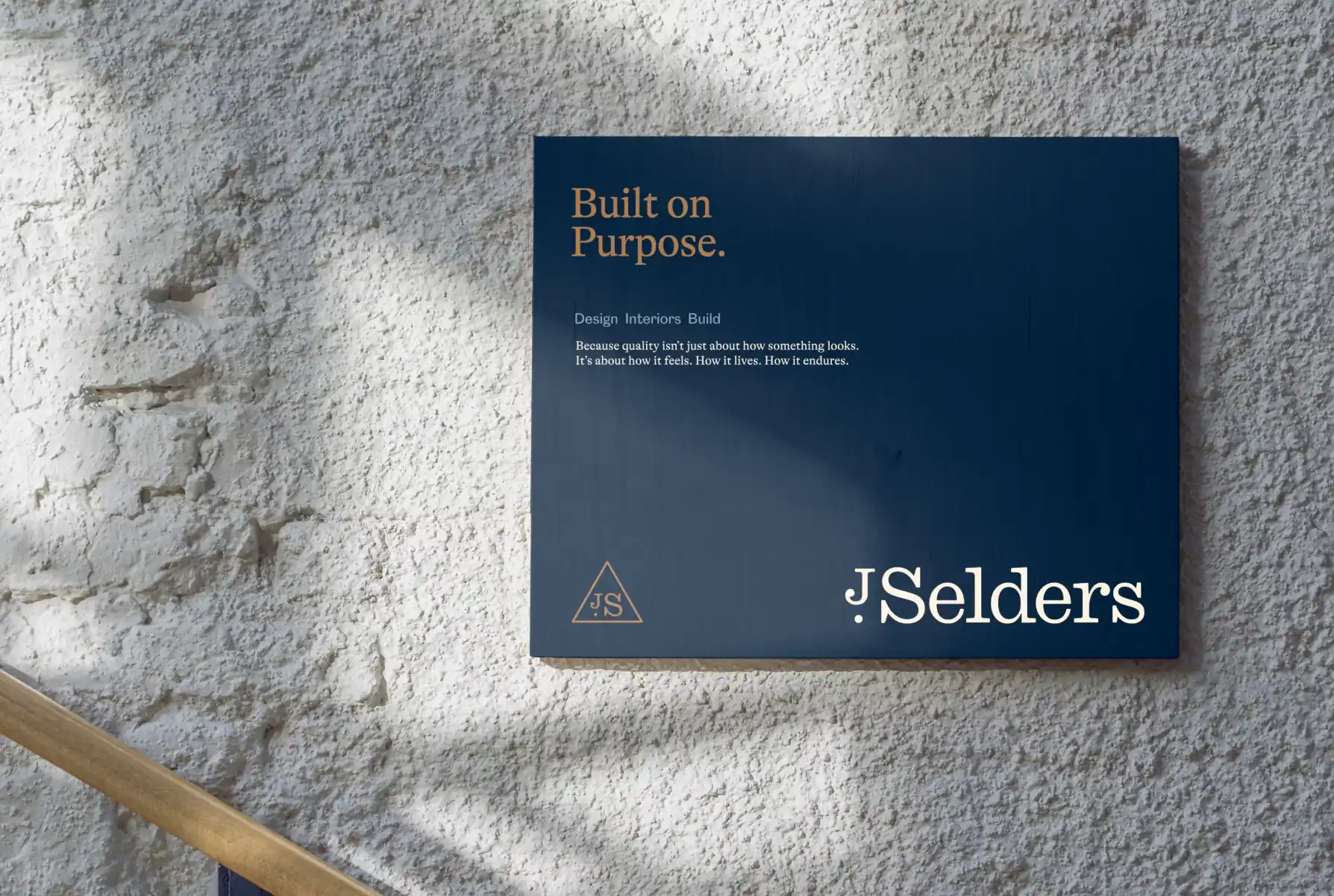 Blue sign on textured wall reading 'Built on Purpose' with additional text about design, interiors, and build by J Selders.