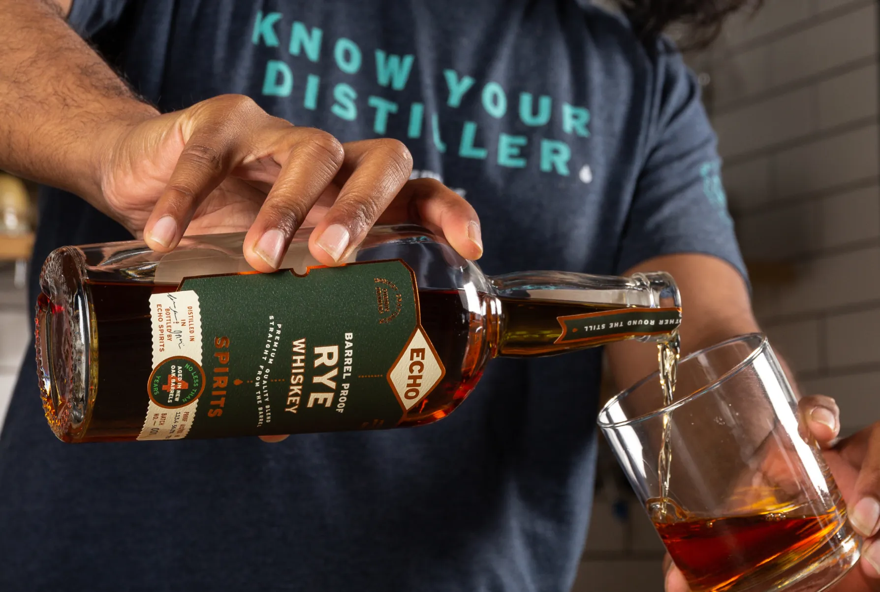 Person pouring amber Echo Spirits Barrel Proof Rye Whiskey from a bottle into a glass.