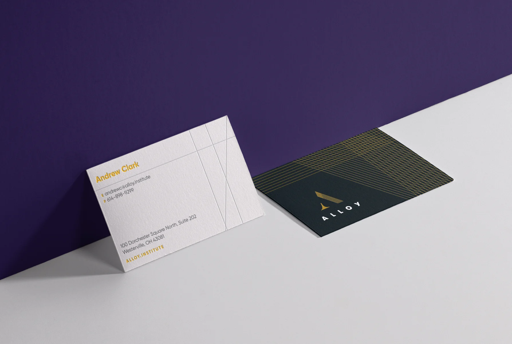 Two Alloy Institute business cards, one showing contact details and the other with a dark background and gold geometric lines and logo.