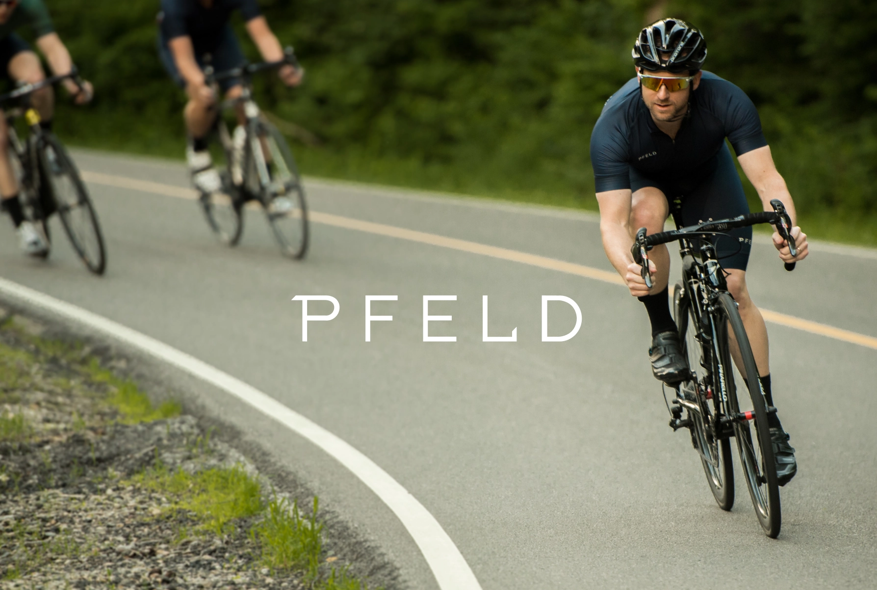 Flat lay of PFELD branded packaging including a thank you card with cyclist photo, product tag, business card, orange candies, and crumpled branded tissue paper on a wooden surface.