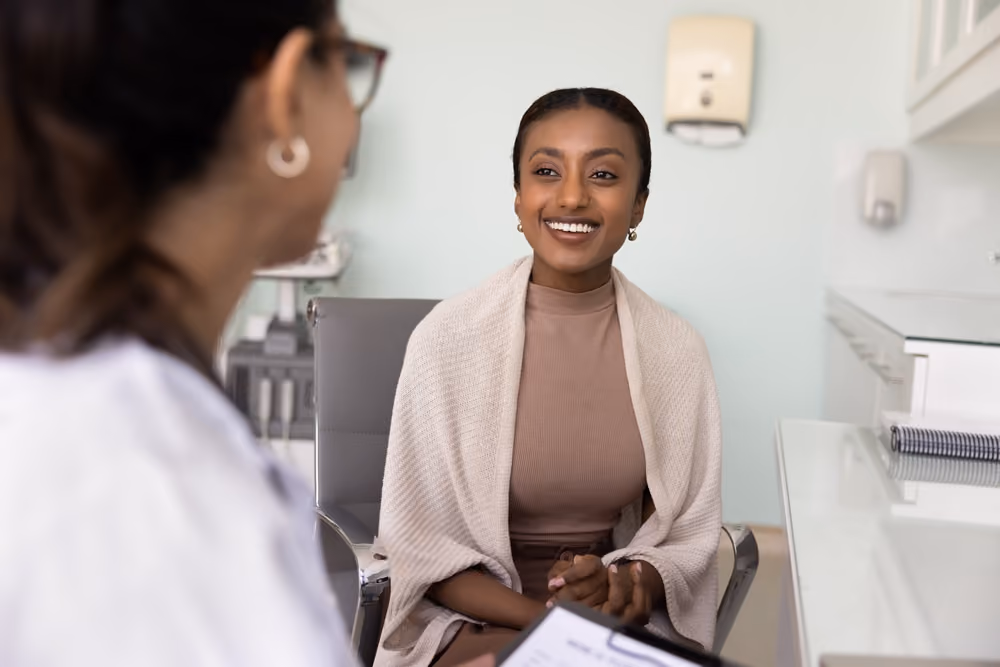 Smiling woman with shawl in a medical office talking with a healthcare professional.