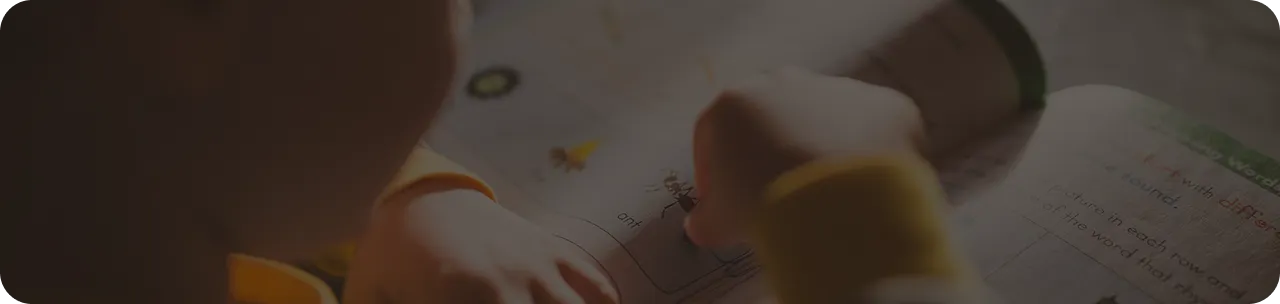 Child writing or coloring in a workbook with an illustration of an ant and the word 'ant'.
