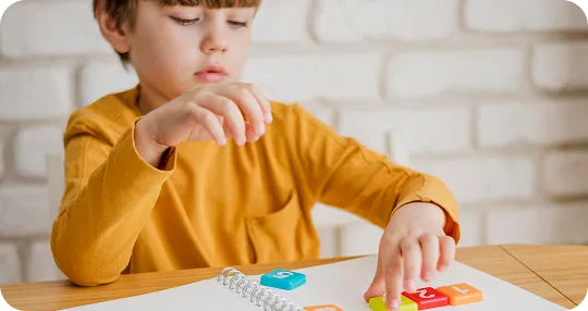 Toddler in blue pajamas reading a colorful picture book on a wooden table in a cozy living room.