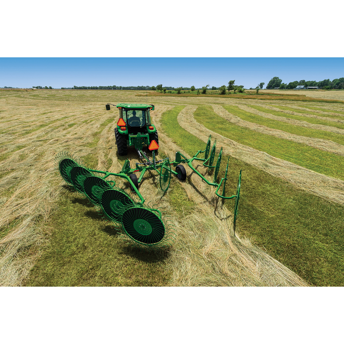 Rear view of a 5M tractor with attached WR0010 Wheel Rake working in a green and tan field