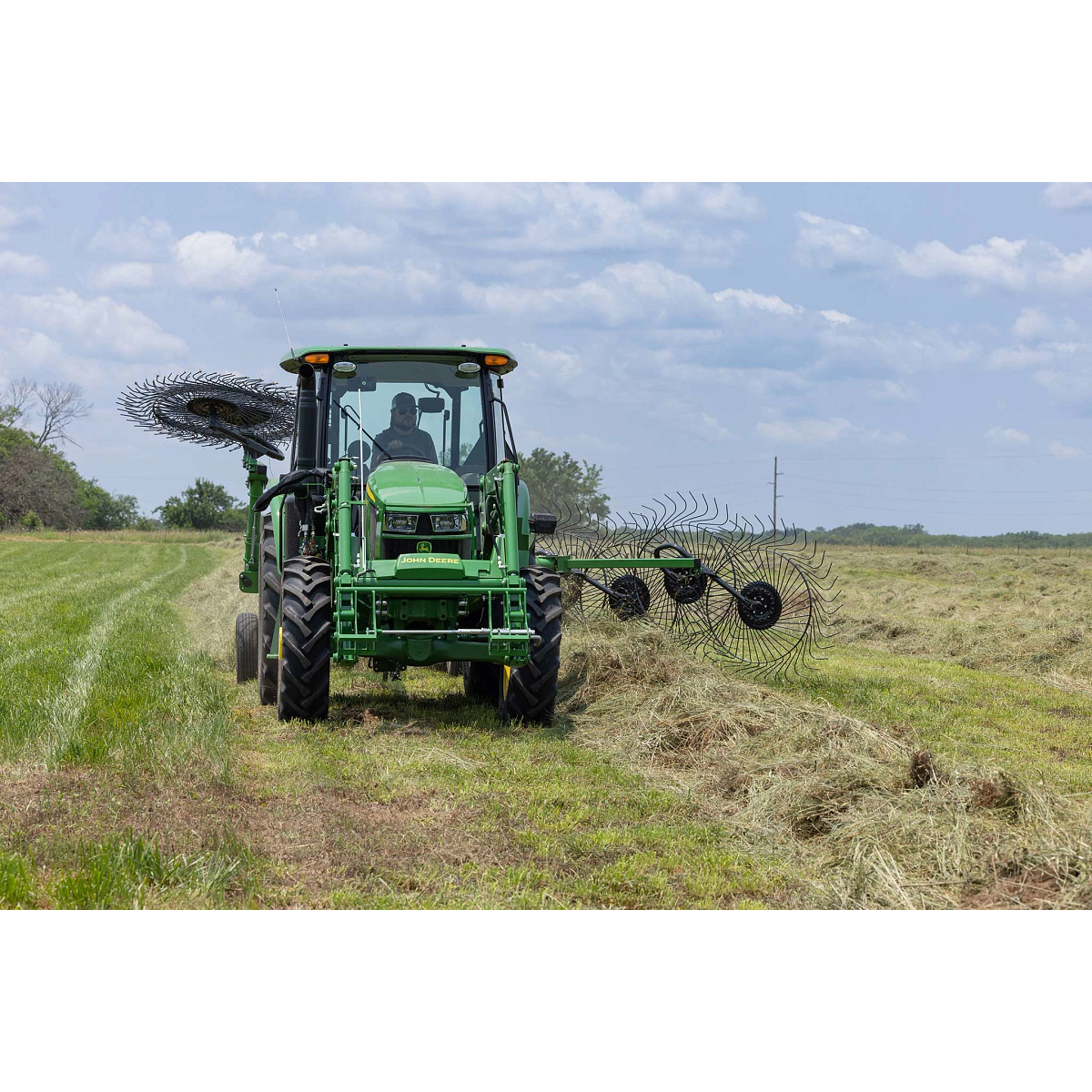 Front view of a 5E series tractor driving along a hay windrow with a WR3212 wheel rake at work behind it