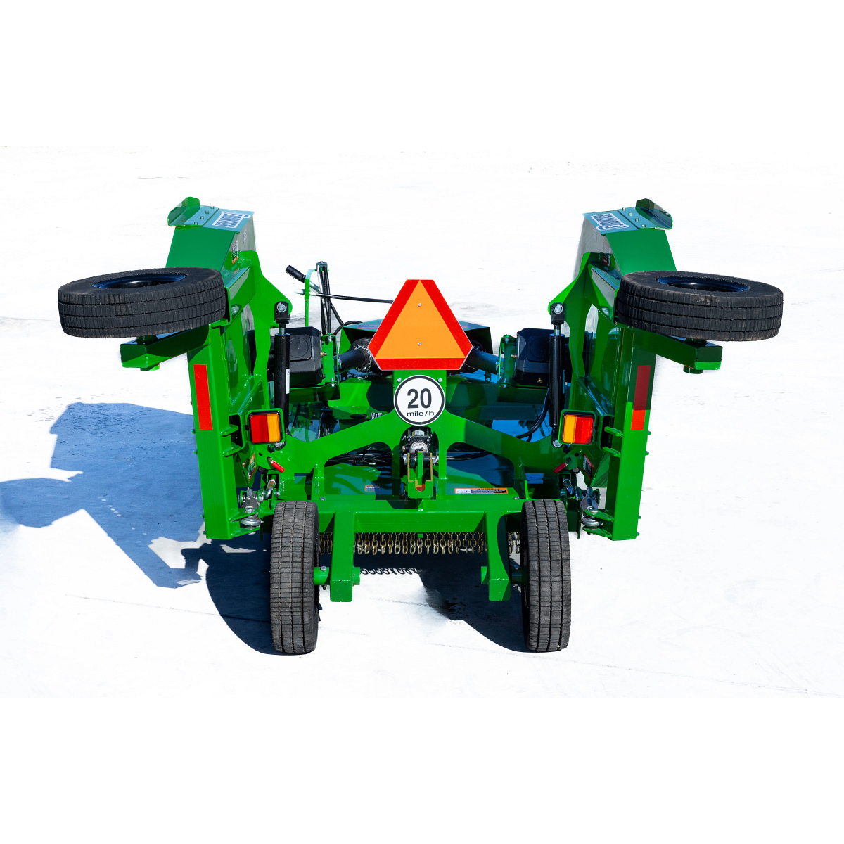 Rear view of a green Frontier rotary cutter in transport position, showing raised wing decks, transport wheels, lights, safety chain shielding, a 20 mph sign, and a slow-moving vehicle emblem on a concrete surface