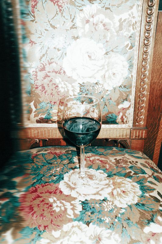 Wine glass filled with red wine placed on a floral-patterned vintage upholstered chair.