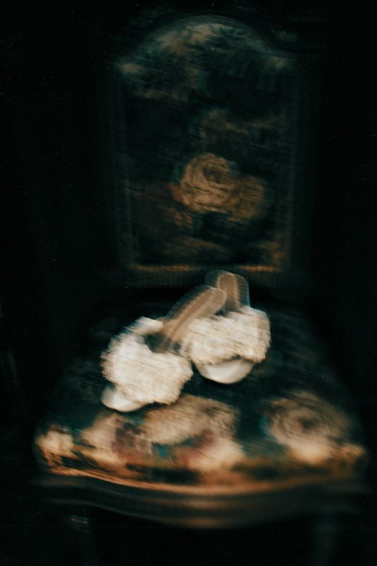 Pair of white fluffy slippers on an ornate vintage chair with floral upholstery.