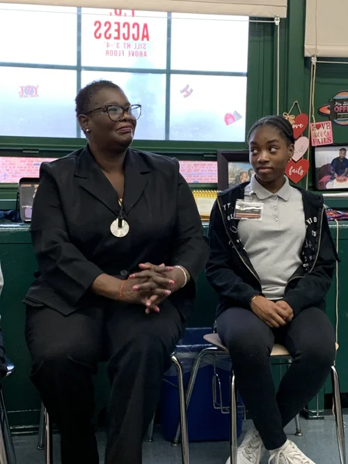 Two people sitting on chairs in a classroom.