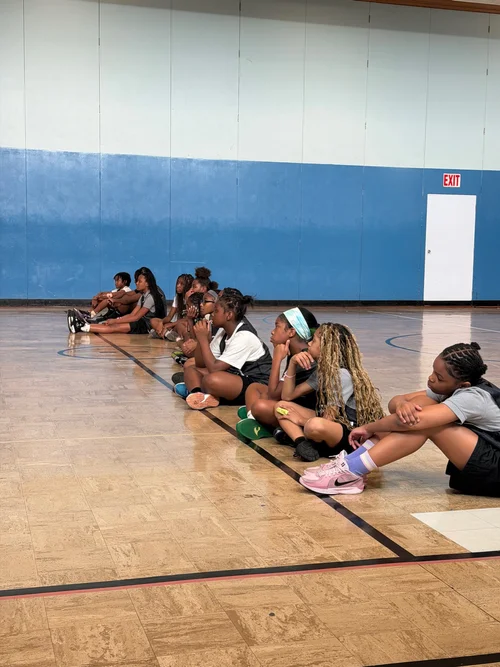 Young girls sitting in a gymnasium along the wall