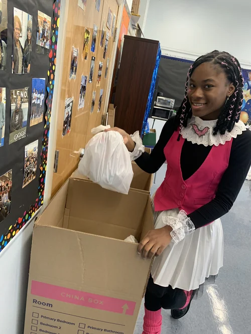 Girl dressed in pink and white placing a bag into a large cardboard box