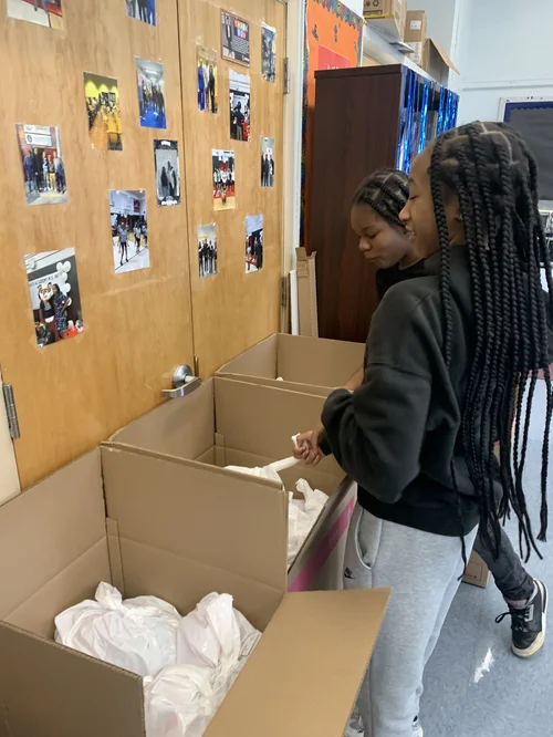 Two girls with braided hair standing by open cardboard boxes.