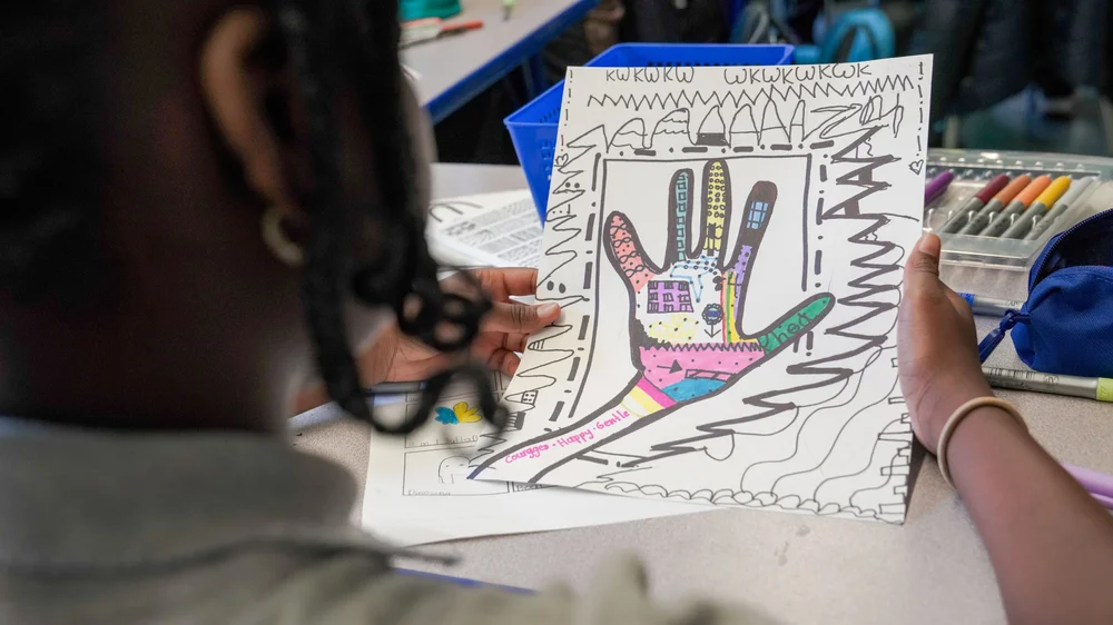 Child holding a colorful hand-drawn artwork featuring a decorated hand outline