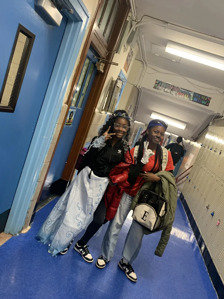 Two young women posing in a school hallway with lockers.