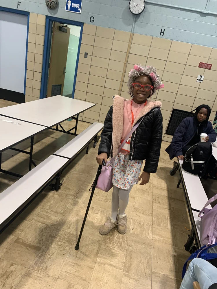 Smiling child indoors with curlers in hair, red glasses.