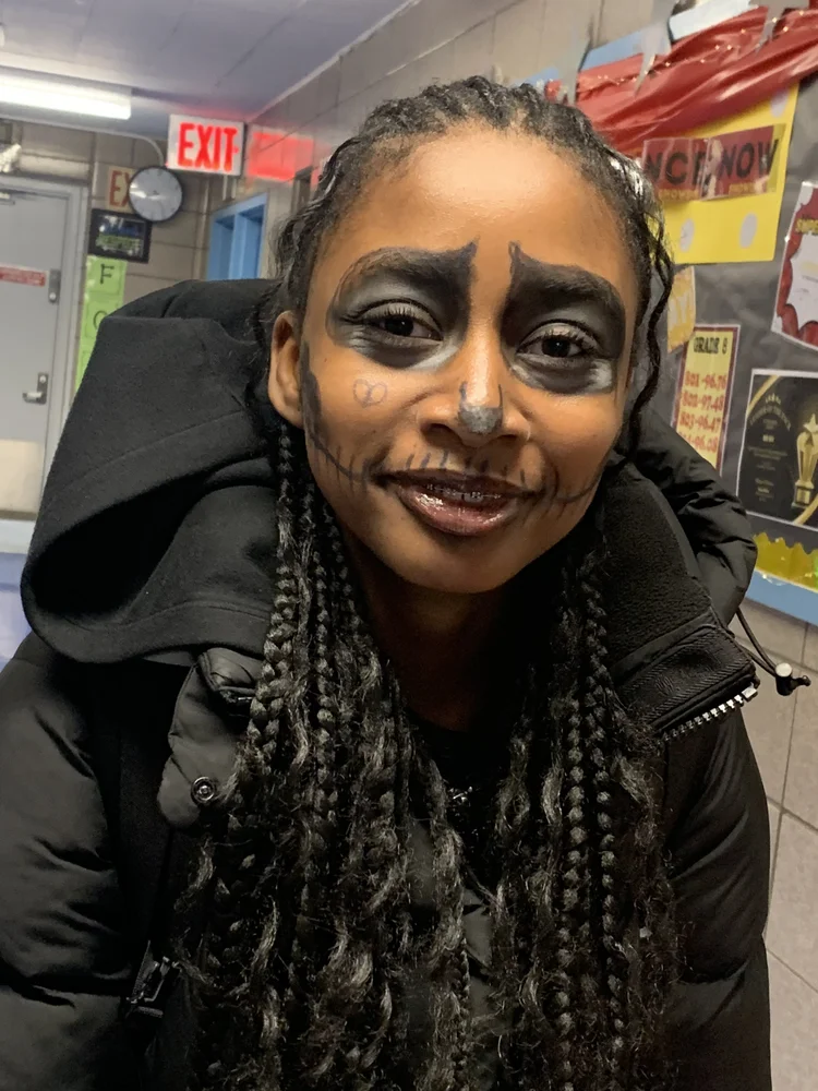 Person with braided hair wearing black jacket and face painted 