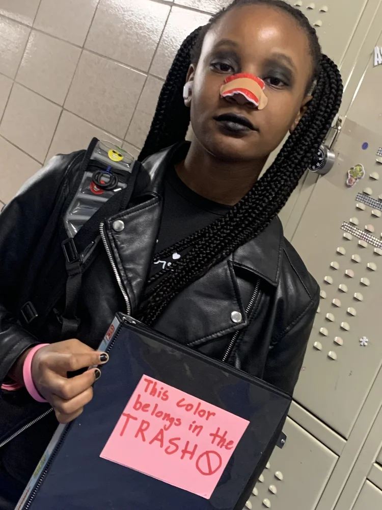 Person with braided hair, black leather jacket, black lipstick, and a red 