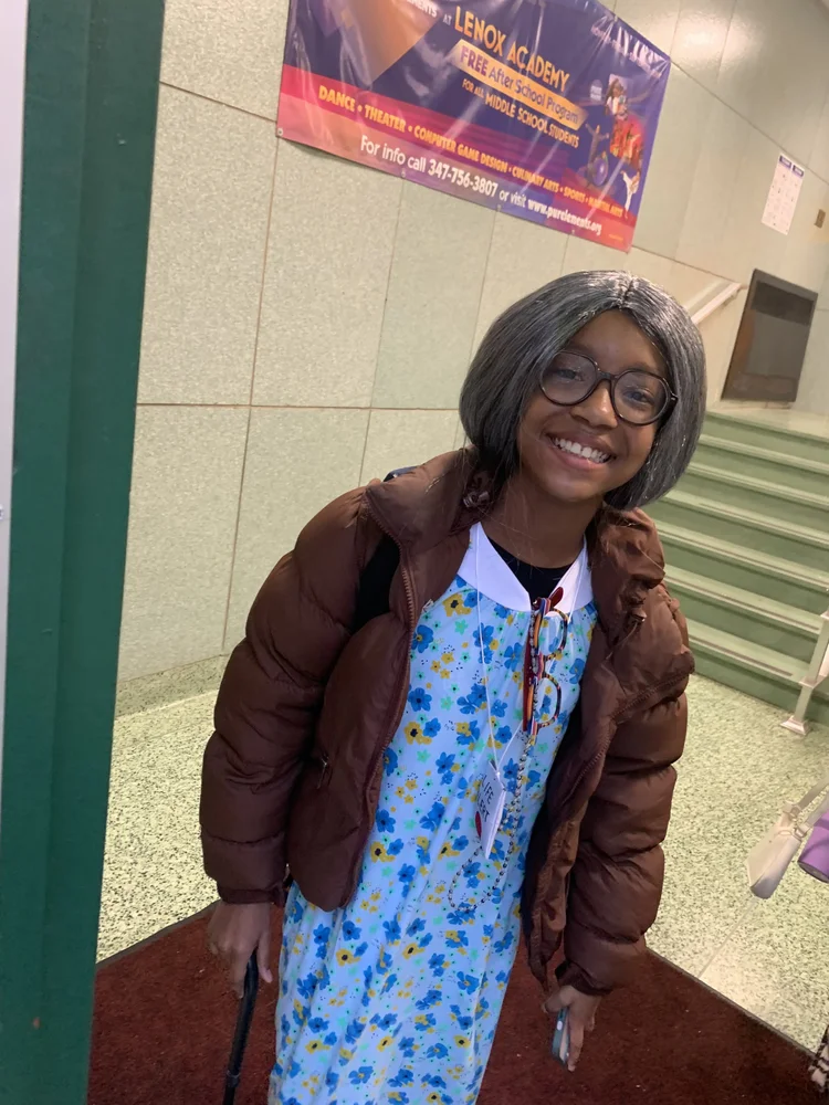 Smiling girl with gray wig, glasses, brown jacket