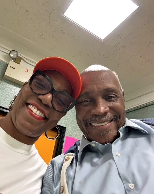 Smiling man in blue shirt and woman wearing large glasses 