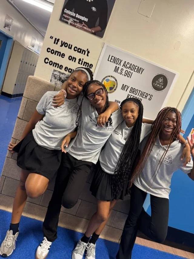 Four smiling teenage girls in school uniforms standing together in a school hallway