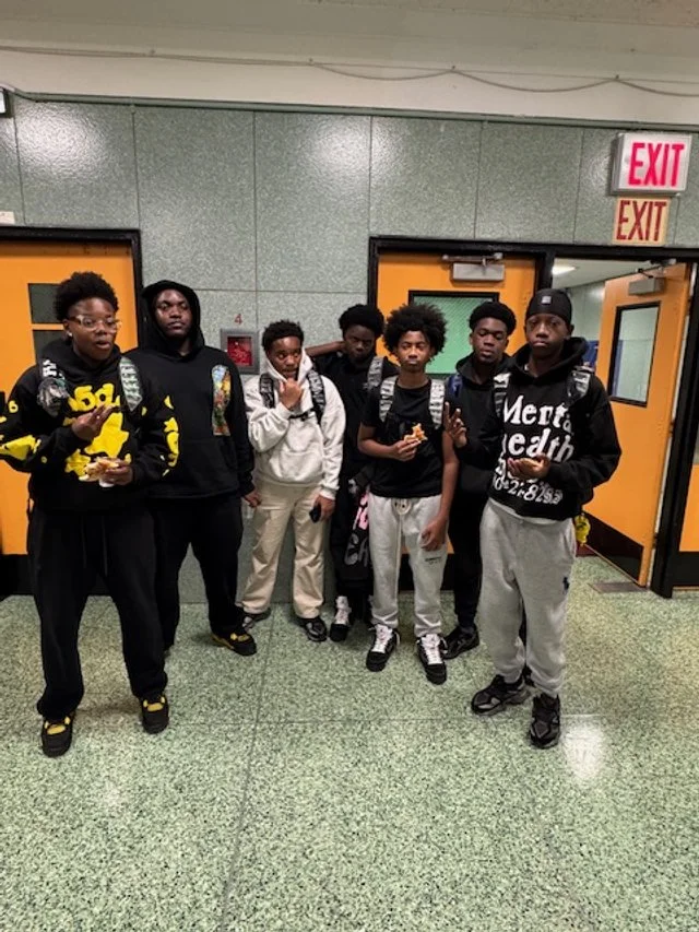 Group of seven teenage boys standing indoors near orange doors 