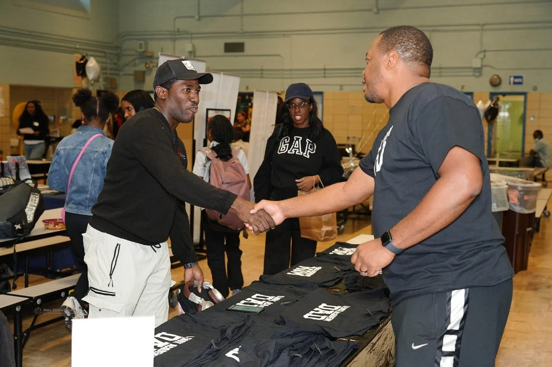 Two men shaking hands over a table with black t-shirts